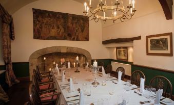 a long dining table is set with white napkins and silverware , surrounded by chairs in a room with a fireplace at The Haycock Manor Hotel
