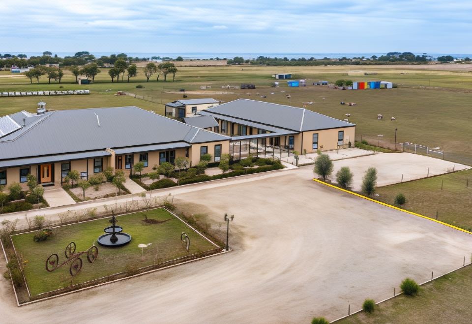 aerial view of a large building surrounded by a grassy field , with a parking lot in front of it at The Oxley Estate