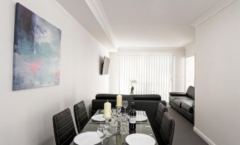 a dining room with a black table set for dinner , surrounded by black leather chairs at East Maitland Executive Apartments