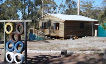 a small wooden cabin situated in a wooded area , surrounded by trees and rocks , with a fence surrounding the property at Gumleaves Bush Holidays