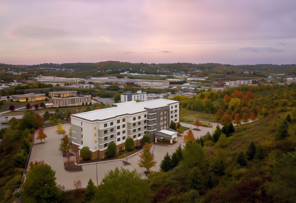 a large , modern building with multiple floors and balconies , situated on a hillside near a city and surrounded by trees at Courtyard Pittsburgh Washington/Meadow Lands