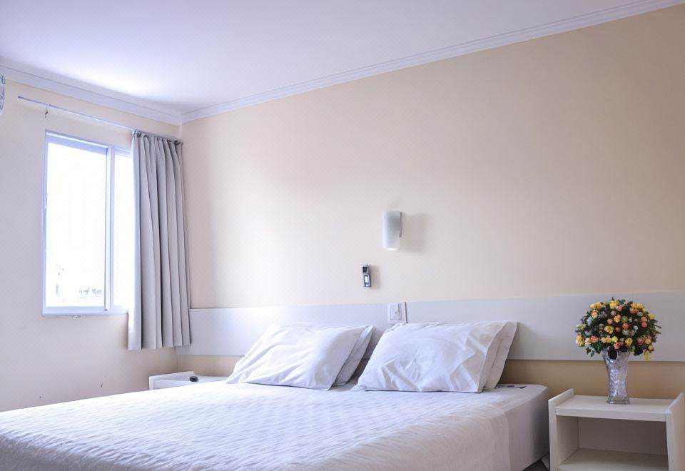 a clean and well - organized hotel room with a white bed , curtains , and a nightstand near the window at Prime Hotel