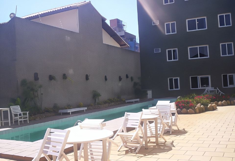 a rooftop pool area with white tables and chairs , surrounded by a black wall and greenery at Hotel du Lac Macae