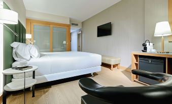 a modern hotel room with a white bed , black leather chair , and a flat screen tv on the wall at Hesperia Barcelona Sant Just
