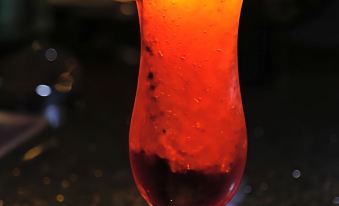 a tall glass filled with a red drink garnished with a lime wedge and mint leaves at Mondo Hotel