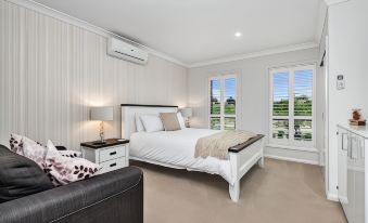 a large bedroom with a white bed , black couch , and a view of the outdoors through the large windows at The Oxley Estate