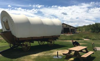 a wooden covered wagon is parked in a grassy field with a picnic table nearby at BlissWood B&B Ranch