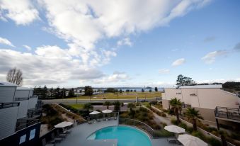 a large pool is surrounded by lounge chairs and tables , with a view of the ocean in the background at Corrigans Cove