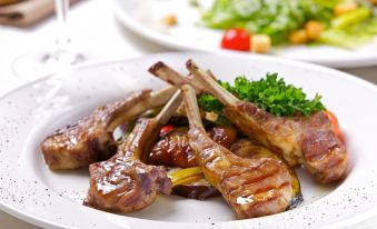 a white plate with several pieces of grilled lamb chops on it , accompanied by a salad at Greenwood Hotel