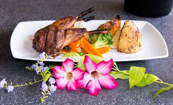 a plate of food with meat , vegetables , and potatoes is displayed on a table with a flower arrangement at Litchfield Outback Resort