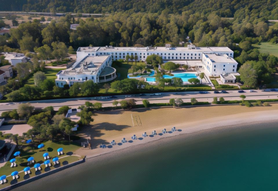 aerial view of a large hotel on a beach , surrounded by trees and water , with several people enjoying the resort at Mitsis Galini