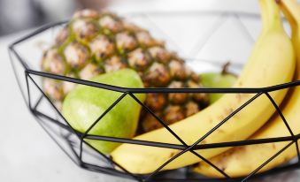 a close - up of a metal wire basket filled with various fruits , including apples , bananas , and pineapples at Aspire Mayfield