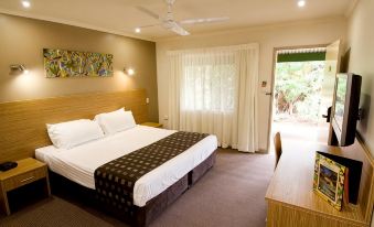 a large bed with a brown and white blanket is in a room with a desk and a sliding glass door at Cairns Colonial Club Resort