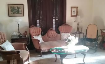 a cozy living room with a pink couch , a coffee table , and a window with shutters at Smithville Historical Museum and Inn