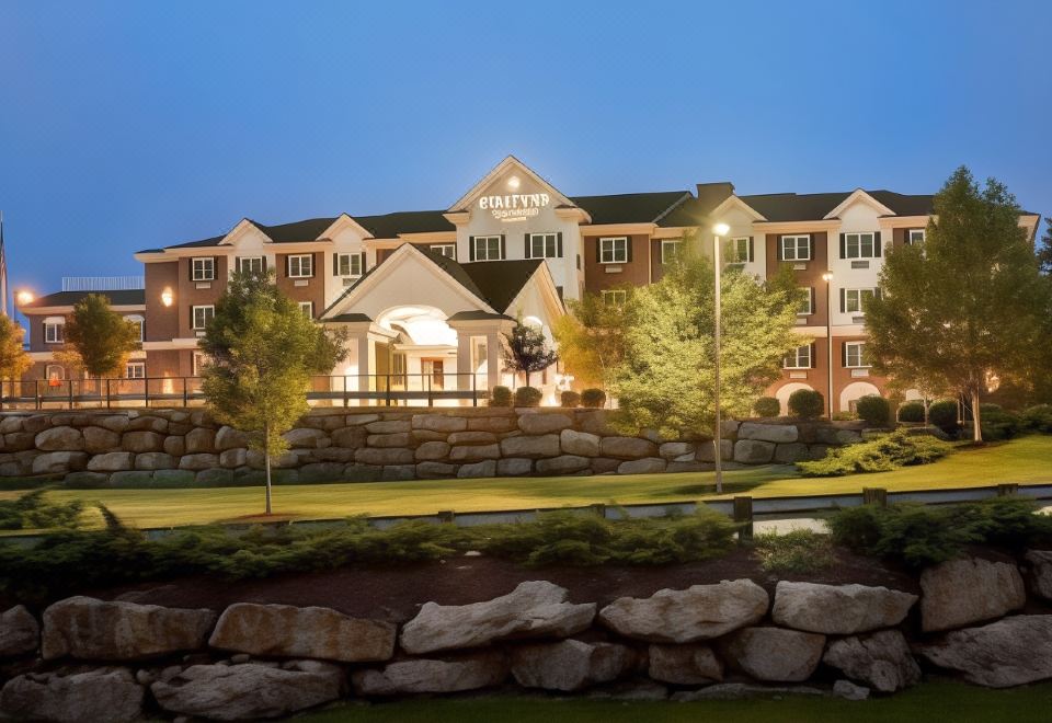 "a large , white hotel building with the name "" patriots lodge "" lit up at night , surrounded by a well - maintained garden and stone wall" at Country Inn & Suites by Radisson, Manchester Airport, NH