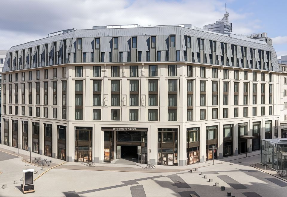 a large , modern building with a curved facade and many windows is surrounded by a plaza at NH Leipzig Zentrum