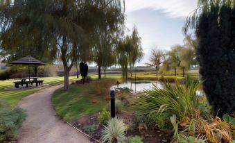 a park with a pond , trees , and bushes is shown in the foreground , while a person is standing near the water at Grosvenor Pulford Hotel & Spa