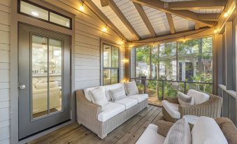 a wooden porch with a white couch and chairs , surrounded by large windows that offer a view of the outdoors at Magnolia Cottages by the Sea by Panhandle Getaways