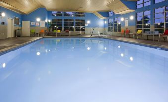 a large , empty swimming pool with blue water and white tiles , surrounded by lounge chairs and windows at Comfort Inn & Suites