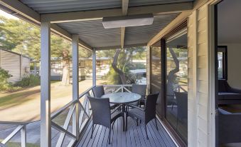 a wooden deck with a table and chairs on it , surrounded by trees and grass at Nrma Sydney Lakeside Holiday Park