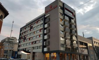 "a large , modern building with the name "" ramada "" prominently displayed on its side , surrounded by other buildings and cars" at Ramada by Wyndham Ramnicu Valcea