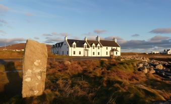 a white house with a stone pillar in front of it , set against a blue sky at Polochar Inn