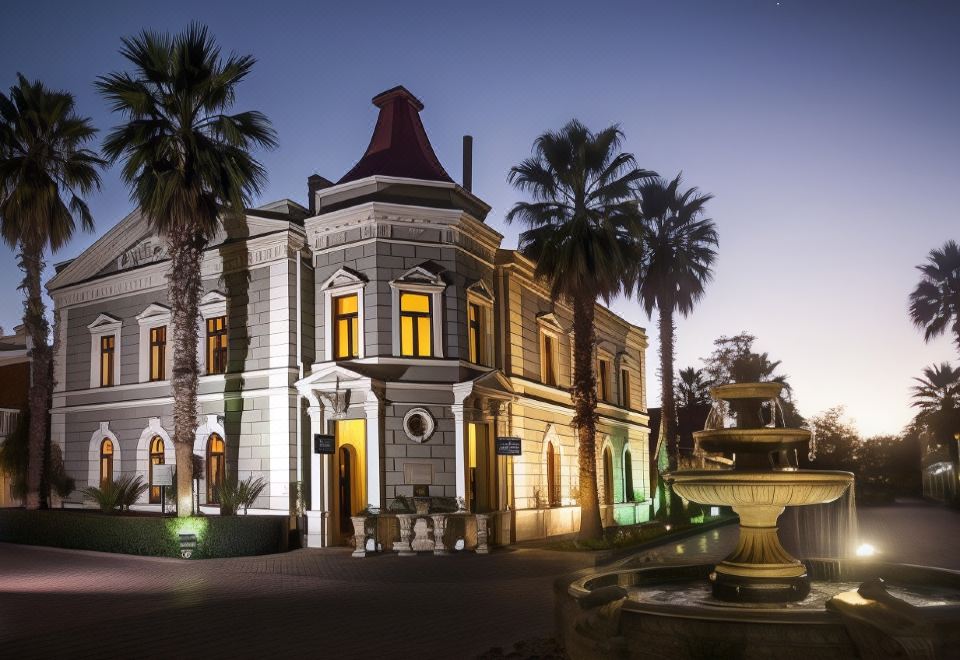 a large , ornate building with a red roof is surrounded by palm trees and has a fountain in front at Gold Reef City Theme Park Hotel