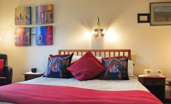 a bed with a wooden headboard and red bedding , flanked by two decorative pillows and a wall - mounted light at Ashcroft Farmhouse