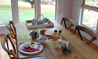 a wooden dining table is set with a breakfast spread including eggs , bacon , toast , and tea at Abby's Cottages