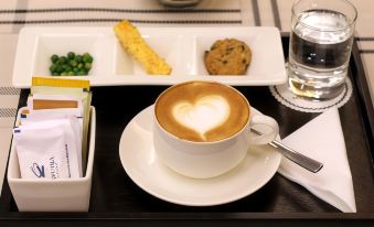 a cup of coffee with a heart - shaped design on the foam is placed on a saucer next to other items at Hotel Ciputra Cibubur Managed by Swiss-Belhotel International