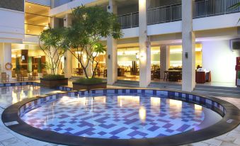 a large outdoor pool is surrounded by a building with windows and has a building in the background at Bueno Colombo Hotel Yogyakarta