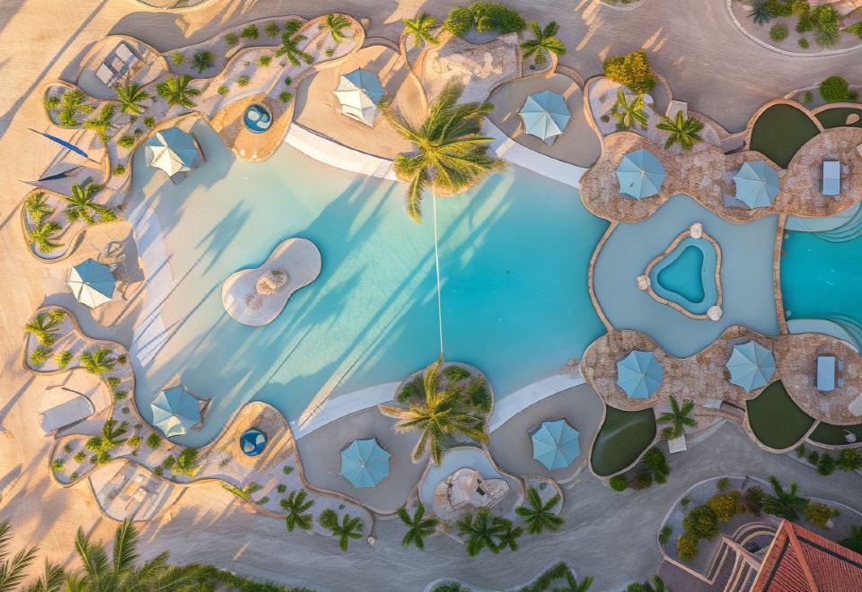 a large , circular pool with blue water and palm trees surrounding it , creating a serene and inviting atmosphere at Coco Beach Resort