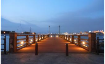 a wooden pier with a lighted railing at dusk , leading to a city skyline in the background at Route Inn Grantia Hakodate Ekimae