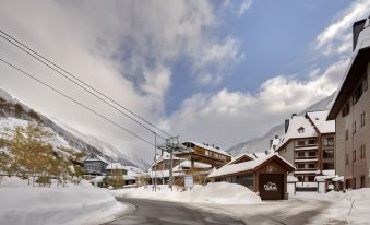 "a snowy mountainous landscape with buildings and ski lifts , as well as a sign for "" villa "" in the foreground" at Hotel Val de Neu G.L.