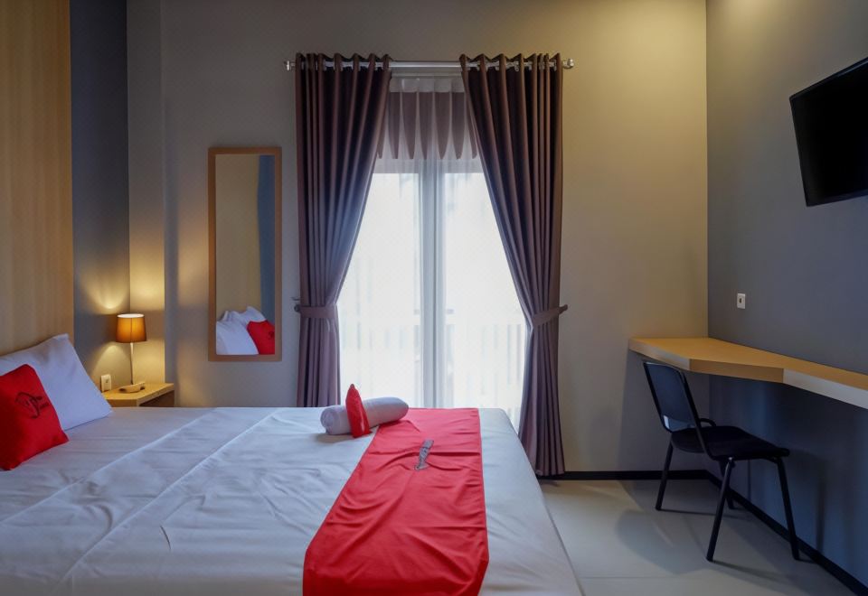 a hotel room with a red bed , curtains , and a desk near the window , illuminated by lights at RedDoorz Syariah @ Jalan Sultan Agung Tegal