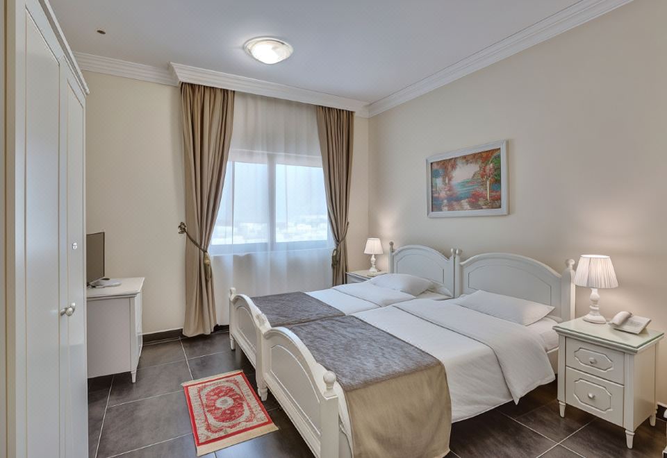 a well - lit hotel room with two beds , white curtains , and a red rug , along with a window and nightstand at Royal Hotel