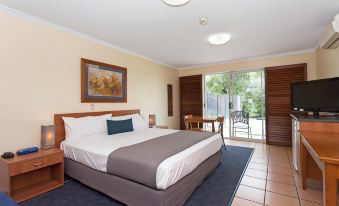 a large bed with a white and gray comforter is in a room with a sliding glass door at Windmill Motel and Events Centre