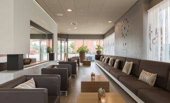 a modern lounge area with gray couches and chairs , a coffee table , and large windows at Leonardo Hotel Papendrecht