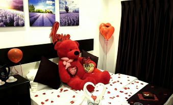 a teddy bear with a heart - shaped balloon on top is sitting on a bed next to a red heart at Hotel Lavender Senawang