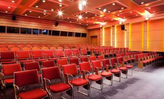 a large conference room with rows of red chairs arranged in a semicircle , creating an auditorium - like setting at Novotel Marne-la-Vallée Noisy-Le-Grand
