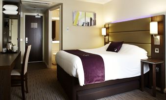 a large bed with a purple and white blanket is in a hotel room next to a door at Premier Inn Derby East