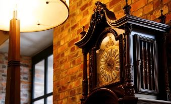 a large wooden clock is hanging on a brick wall with a lamp above it at La Vista Hakodate Bay