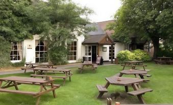 a grassy area with several wooden picnic tables and benches , providing a pleasant outdoor seating area at Premier Inn Lichfield North East (A38)