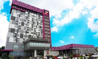 a large building with a pink and gray facade is surrounded by cars parked in front of it at Grand Zuri Dumai