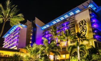 a tall hotel building with blue lights illuminating the exterior , surrounded by palm trees at night at Chateau Royal Beach Resort & Spa, Noumea