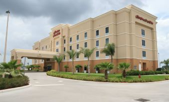 a large hotel with a large sign on the front , surrounded by palm trees and other greenery at Hampton Inn & Suites Lake Wales