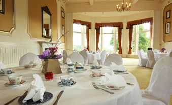 a formal dining room with white tablecloths , floral centerpieces , and plates of food on the table at The Atholl Palace