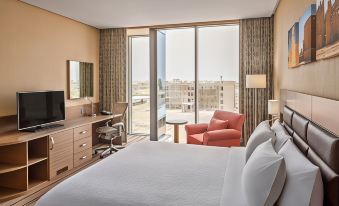 a modern hotel room with a large bed , desk , and orange armchair near a window offering a view of the city at Hilton Garden Inn Tabuk