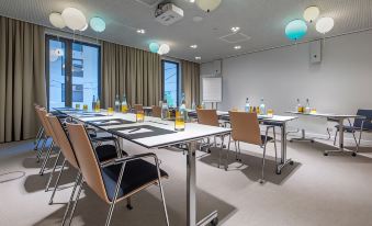 a conference room with a long table and chairs , surrounded by windows and colorful hanging lights at Hilton Garden Inn Mannheim