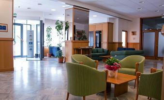 a spacious lobby with green chairs , wooden tables , and potted plants , creating a welcoming atmosphere at Hotel Touring